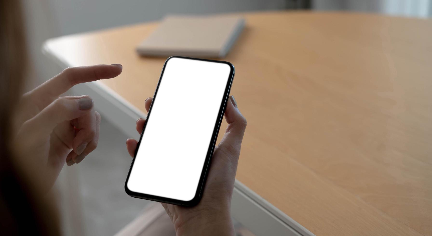 Mockup image blank white screen cell phone.women hand holding texting using mobile on desk at home office. photo