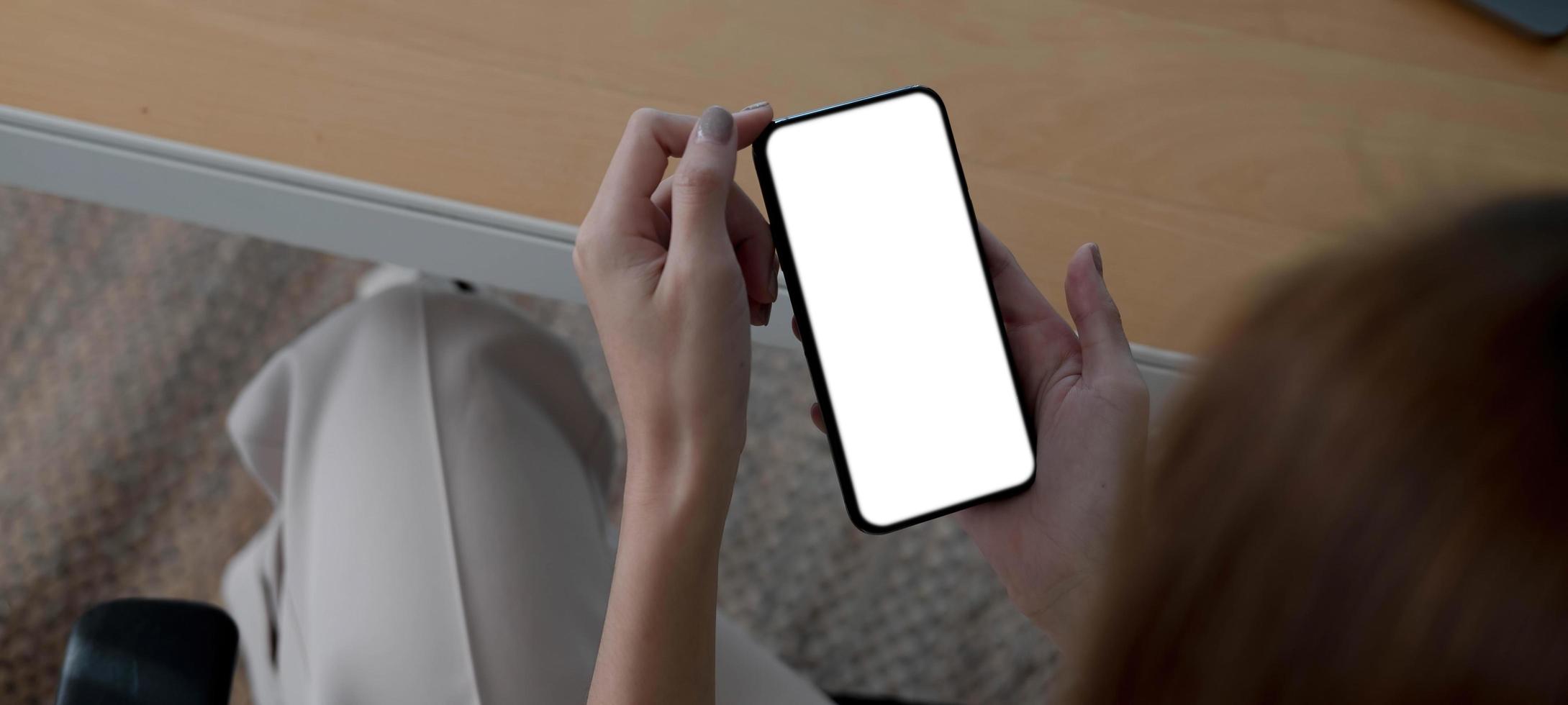 Mockup image blank white screen cell phone.women hand holding texting using mobile on desk at home office. photo