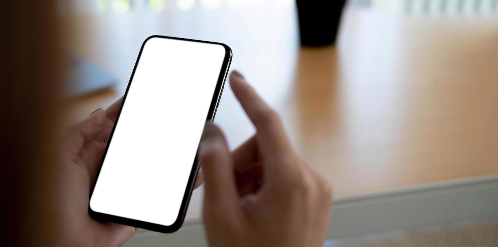 Imagen de maqueta en blanco teléfono celular con pantalla blanca. Mano de mujer sosteniendo mensajes de texto usando el móvil en el escritorio en la oficina en casa. foto