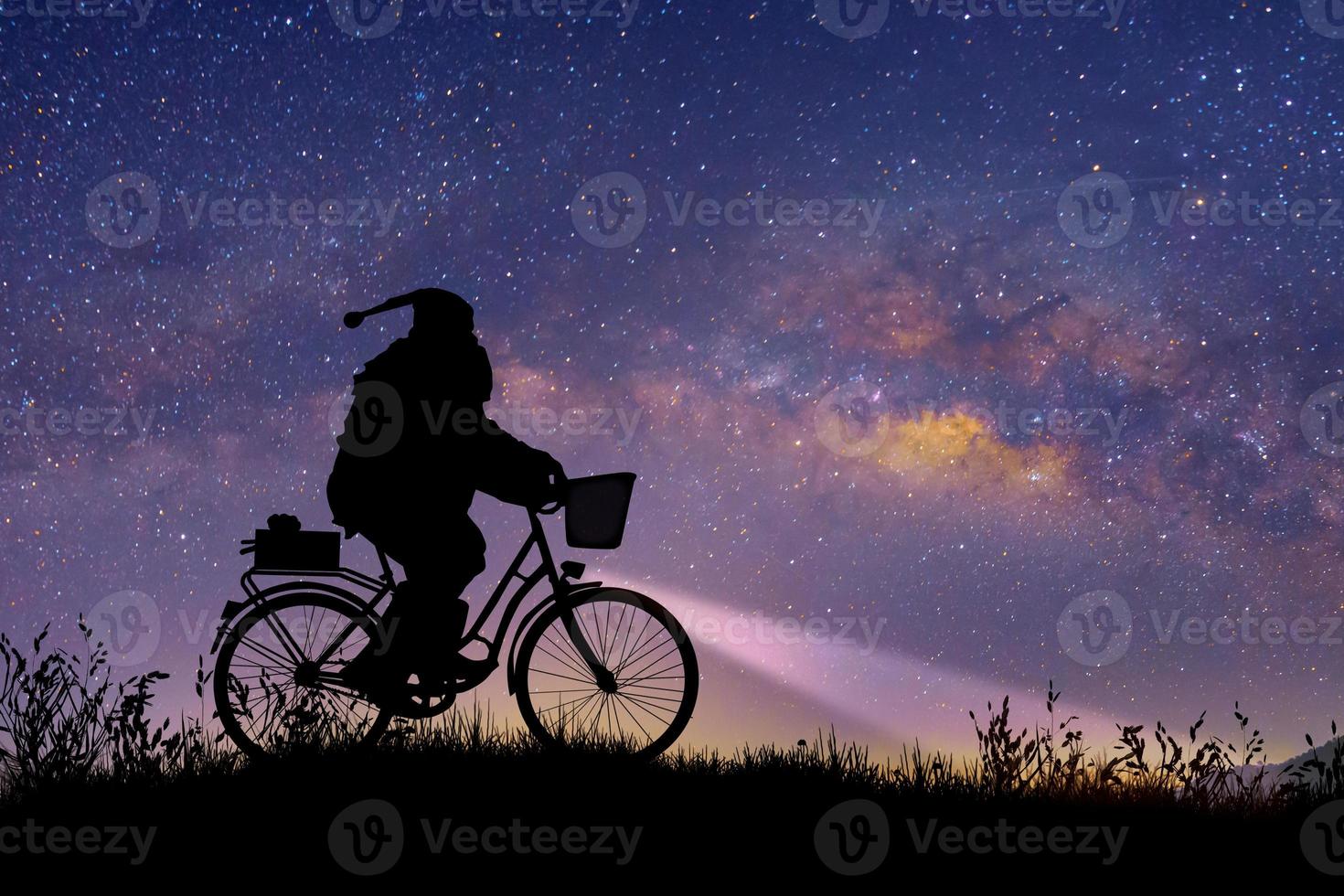 Silhouette of Santa Claus riding on his bicycle to carry a gift under the Milky Way background. photo