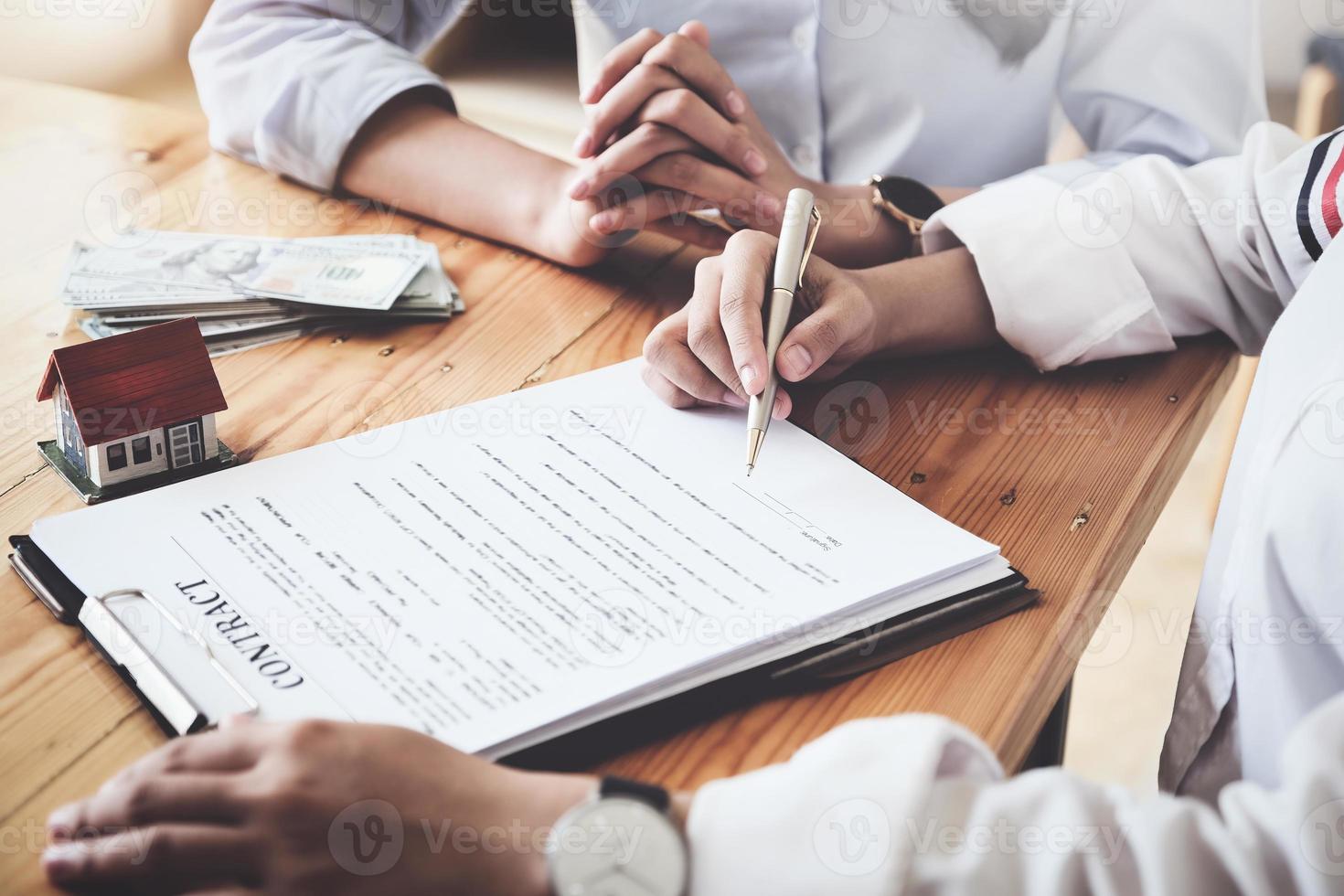 The customer holds a pen and reads the conditions in order to sign a house purchase contract with home insurance documents with the salesperson. photo