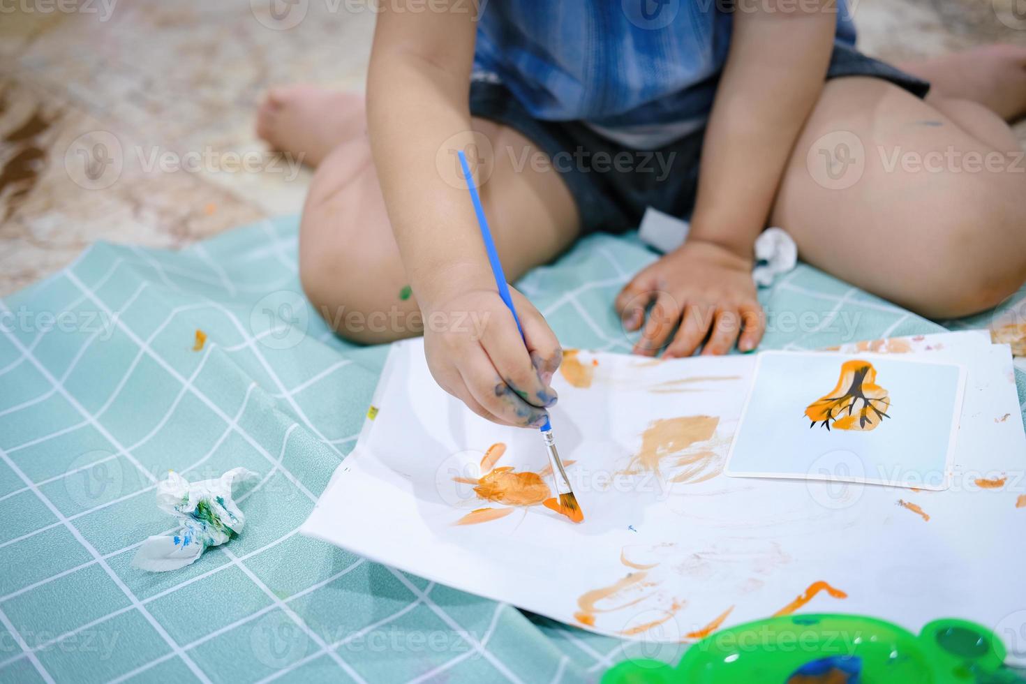 centrarse en las manos sobre el papel. los niños usan pinceles para pintar acuarelas en papel para crear su imaginación y mejorar sus habilidades de aprendizaje. foto