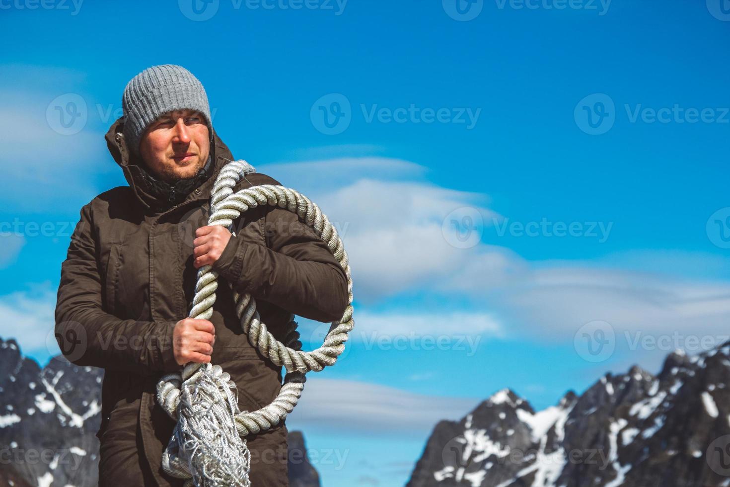 Man with a rope on his shoulder against background of mountains and blue sky photo