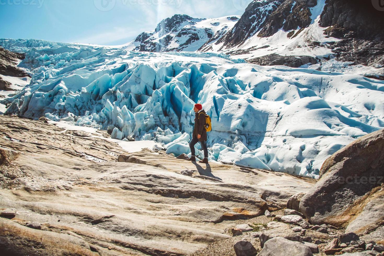 Hombre viajero de pie sobre una roca en el fondo de un glaciar, montañas y nieve foto