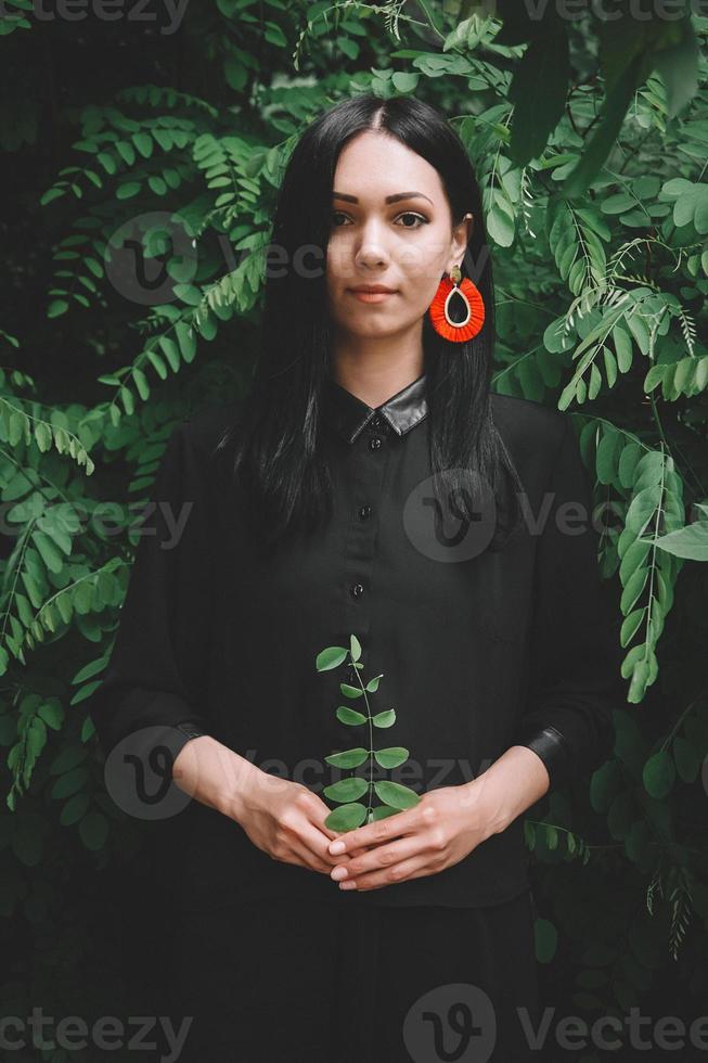 Mujer en vestido negro y adornos rojos sobre fondo de bosque foto