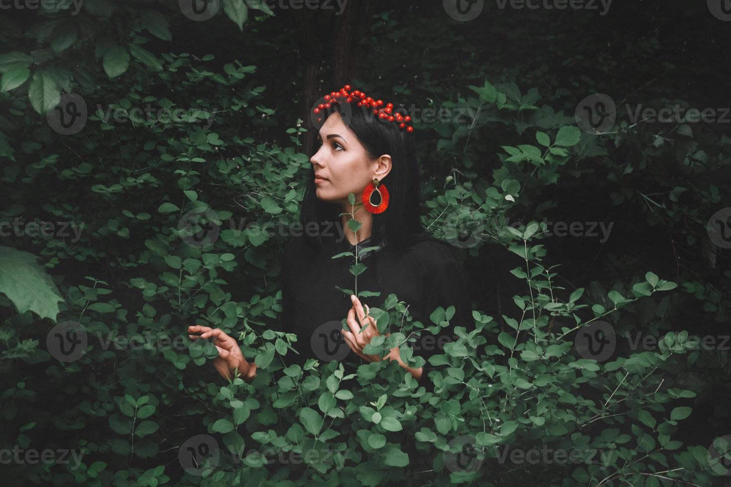 Mujer en vestido negro y adornos rojos sobre fondo de bosque foto