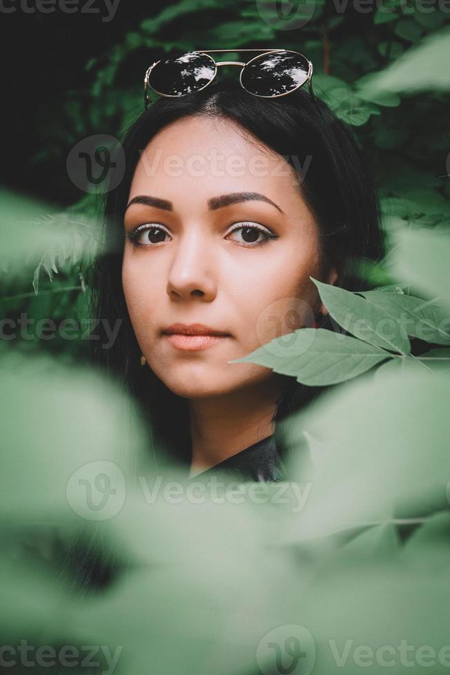 retrato, mujer, en, ropa negra, y, anteojos, contra, plano de fondo, de, hojas verdes foto