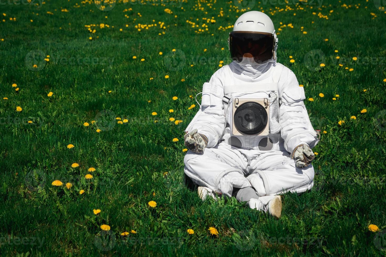 Astronauta futurista en un casco se sienta en un césped verde en una posición meditativa foto