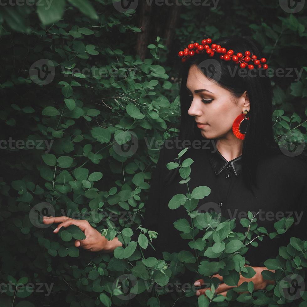 Mujer en vestido negro y adornos rojos sobre fondo de bosque foto