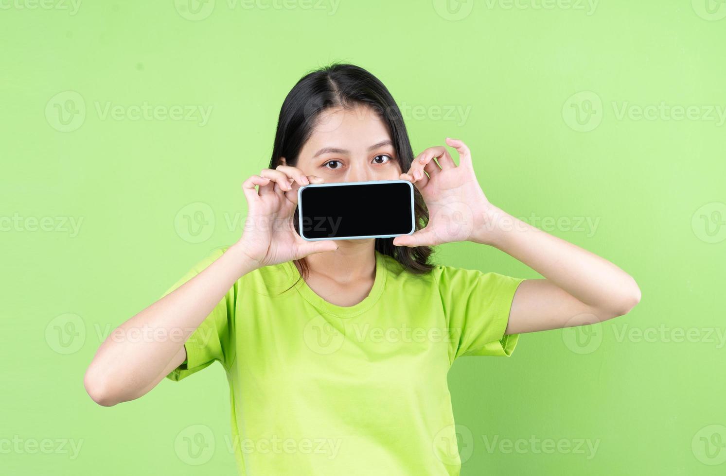 Image of young asian woman holding smartphone on green background photo