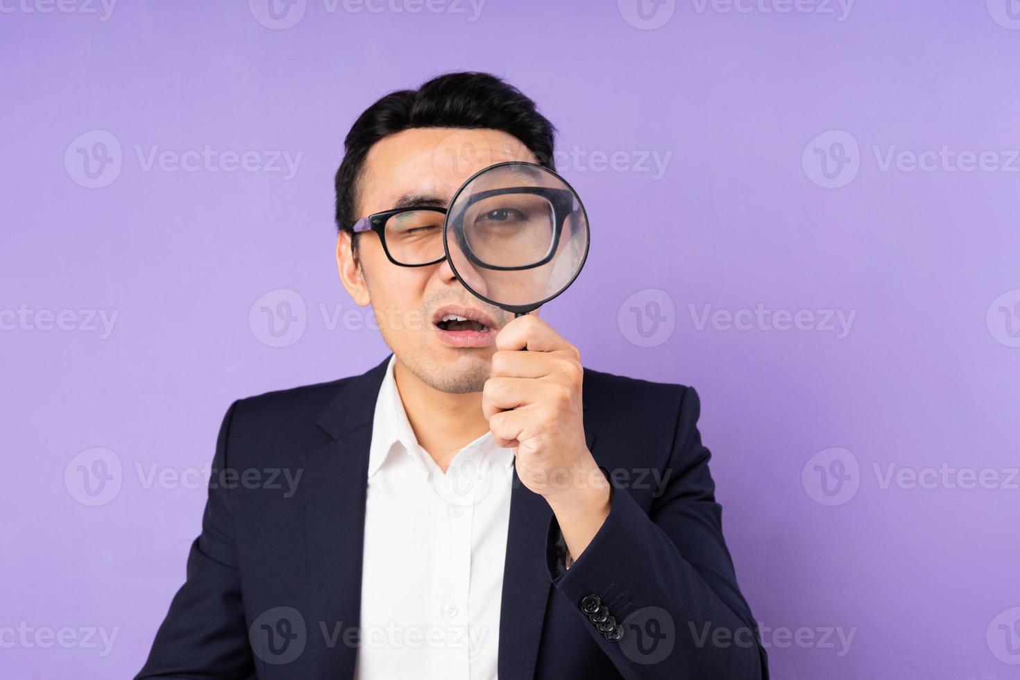 Business man in suit wearing magnifying glass, isolated on purple background photo