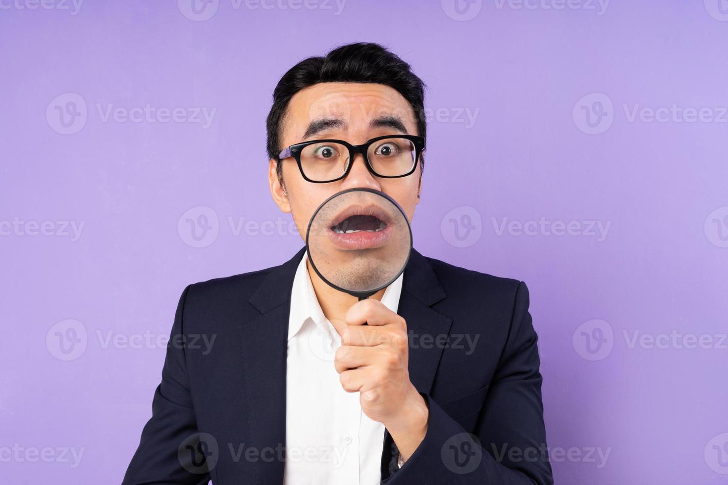 Business man in suit wearing magnifying glass, isolated on purple background photo