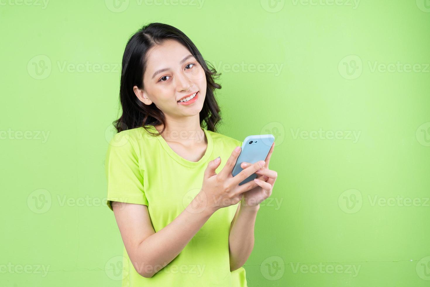 Image of young asian woman holding smartphone on green background photo