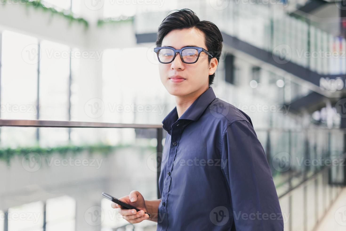 Retrato de un hombre de negocios asiático, confiado y sonriente, sosteniendo un teléfono en la mano foto