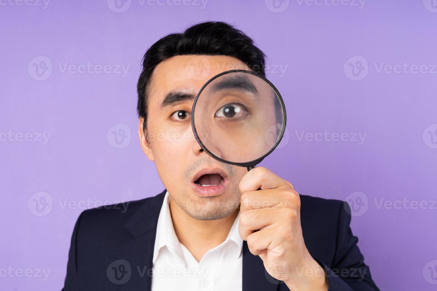 Business man in suit wearing magnifying glass, isolated on purple background photo