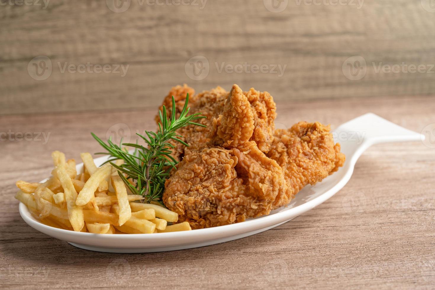 Pollo frito y papas fritas con hojas de romero, comida chatarra alta en calorías servida en un plato blanco foto