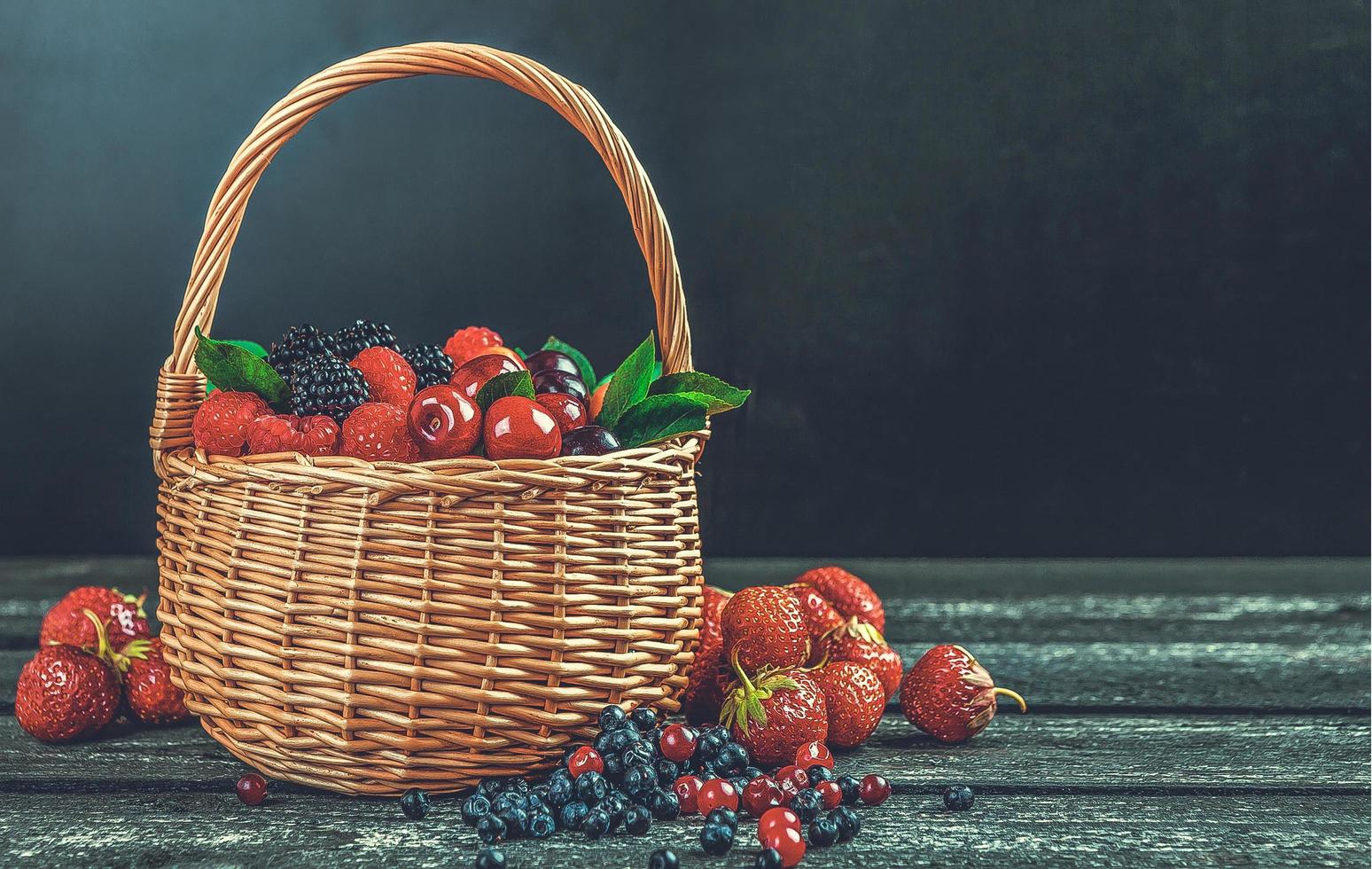 Fresh forest berries in basket on black wooden background with copy space photo