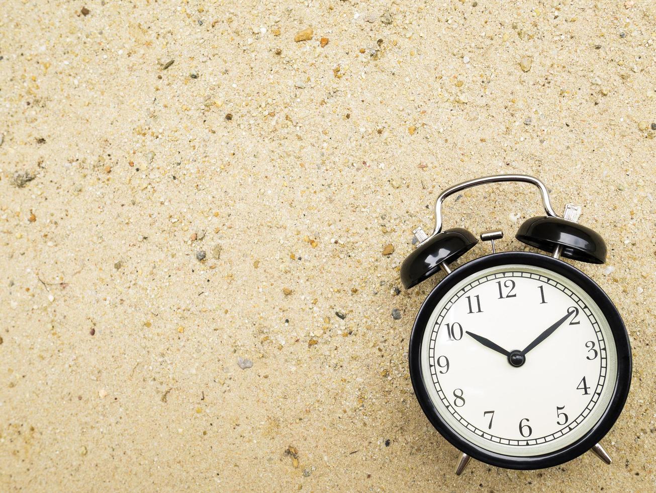 Alarm clock on beach sand, showing ten o'clock photo