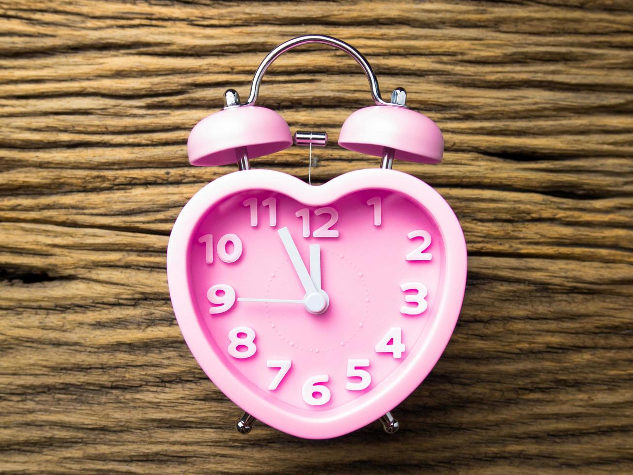 Pink alarm clock in the form of heart on wooden background photo