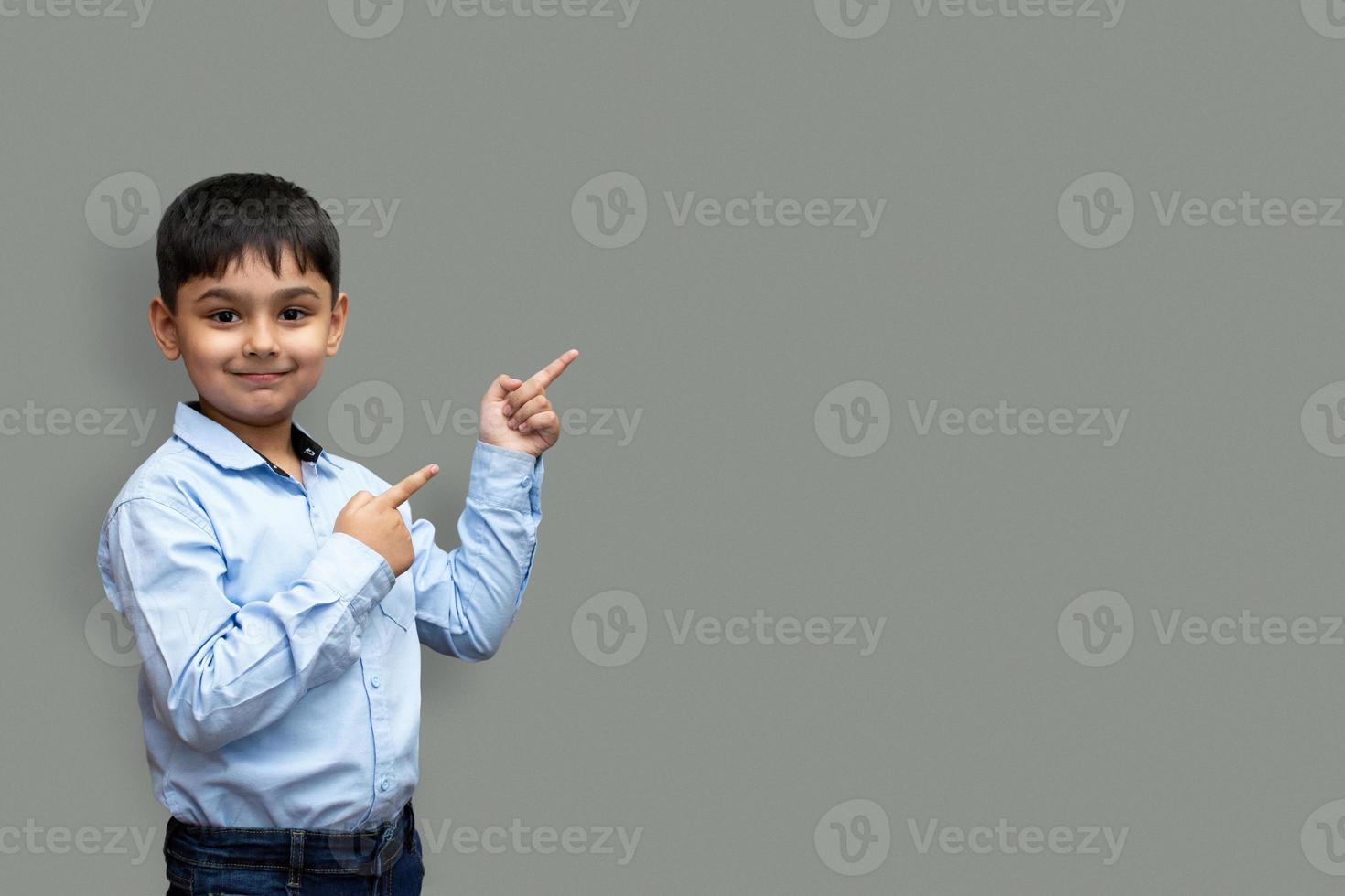 Sonriente niño feliz apuntando con el dedo hacia el espacio de copia aislado sobre fondo liso foto