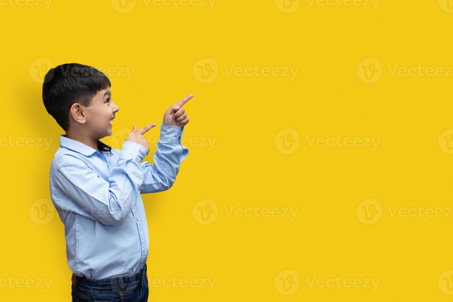 Sonriente niño feliz apuntando con el dedo hacia el espacio de copia aislado sobre fondo liso foto