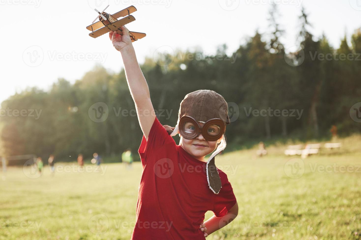 Happy kid in pilot helmet playing with a wooden toy airplane and dreaming of becoming flying photo