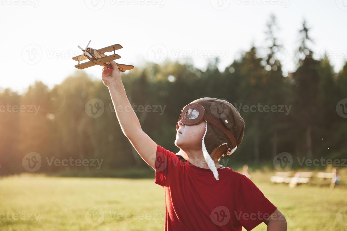Happy kid in pilot helmet playing with a wooden toy airplane and dreaming of becoming flying photo