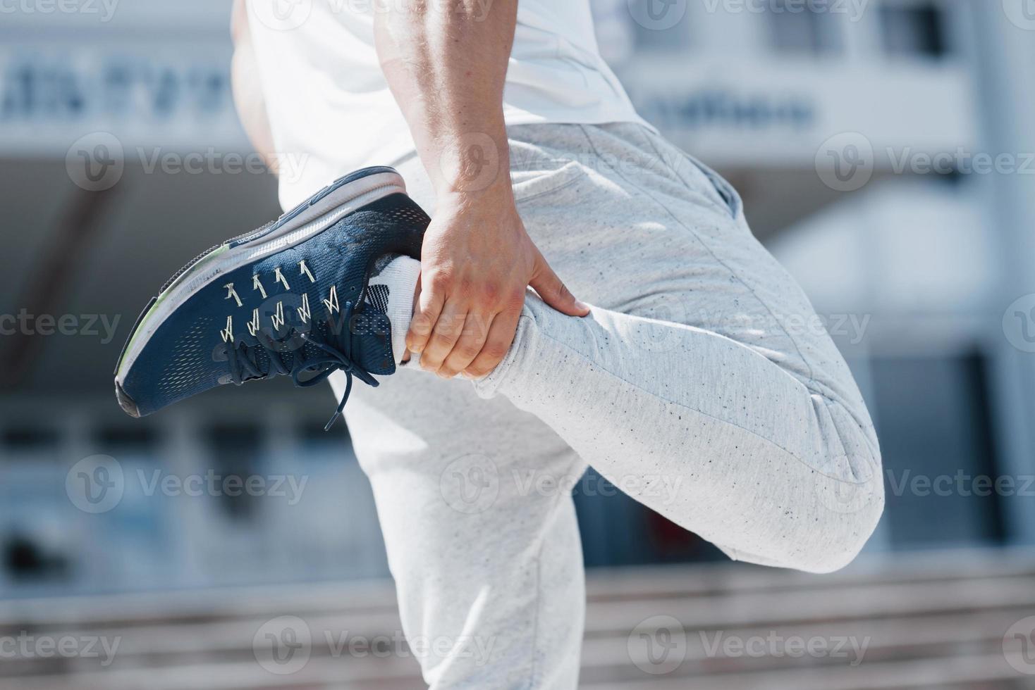 Un apuesto hombre de fitness en ropa deportiva, haciendo estiramientos mientras se prepara para un ejercicio serio en la ciudad moderna foto