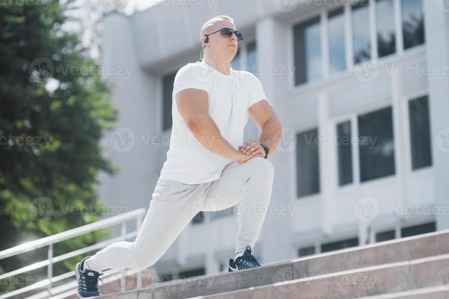 Un apuesto hombre de fitness en ropa deportiva, haciendo estiramientos mientras se prepara para un ejercicio serio en la ciudad moderna foto