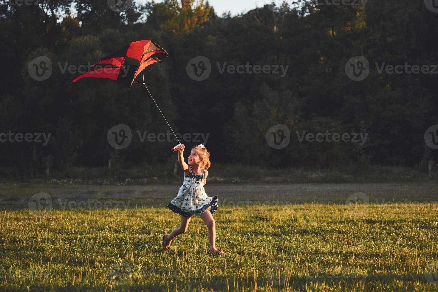 Linda niña con cabello largo corriendo con cometa en el campo en un día soleado de verano foto