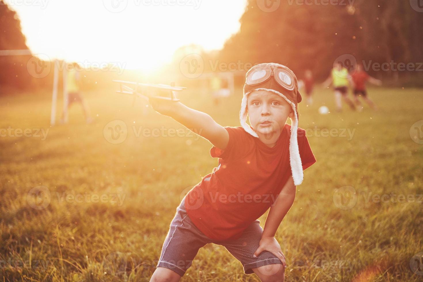 Niño feliz en casco de piloto jugando con un avión de juguete de madera y soñando con volar foto