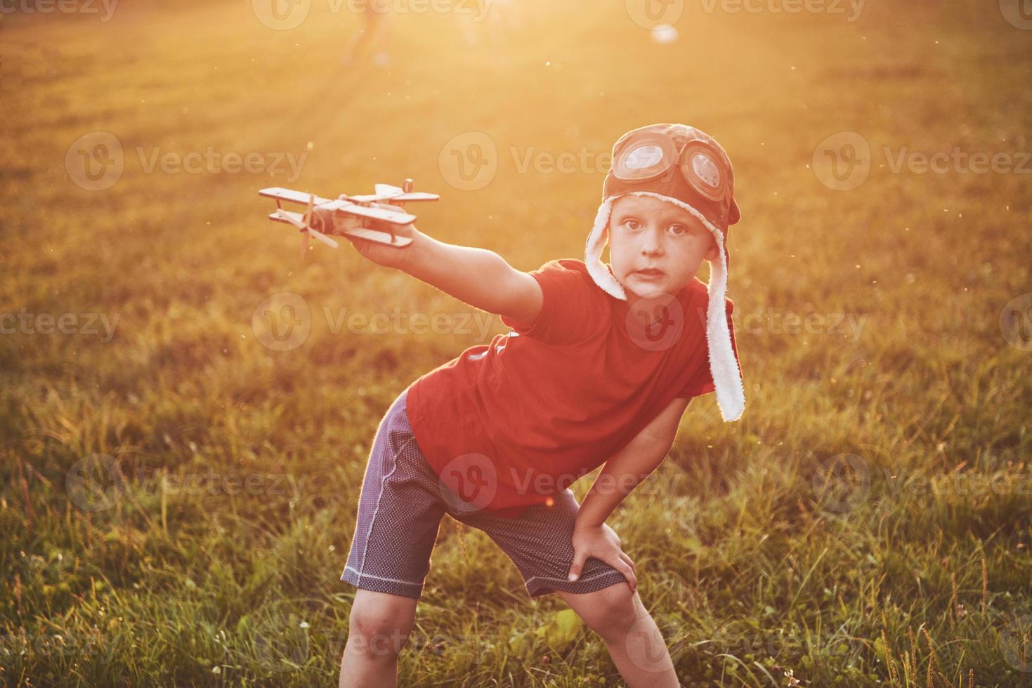 Happy kid in pilot helmet playing with a wooden toy airplane and dreaming of becoming flying photo