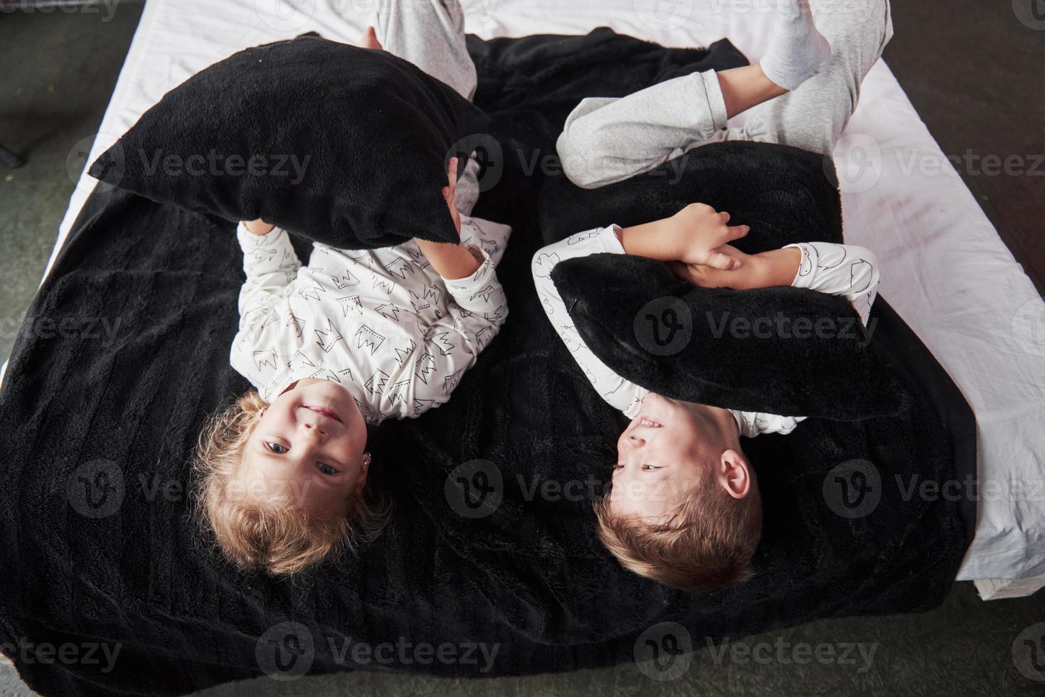 niños traviesos niño y niña organizaron una pelea de almohadas en la cama del dormitorio. les gusta ese tipo de juego foto