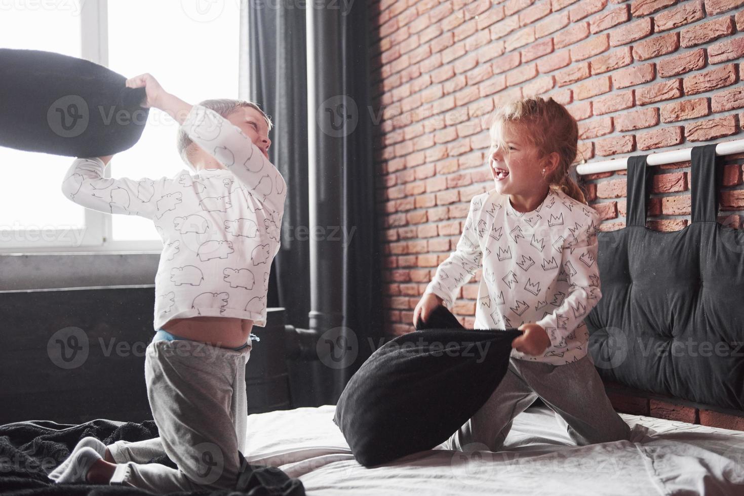 niños traviesos niño y niña organizaron una pelea de almohadas en la cama del dormitorio. les gusta ese tipo de juego foto