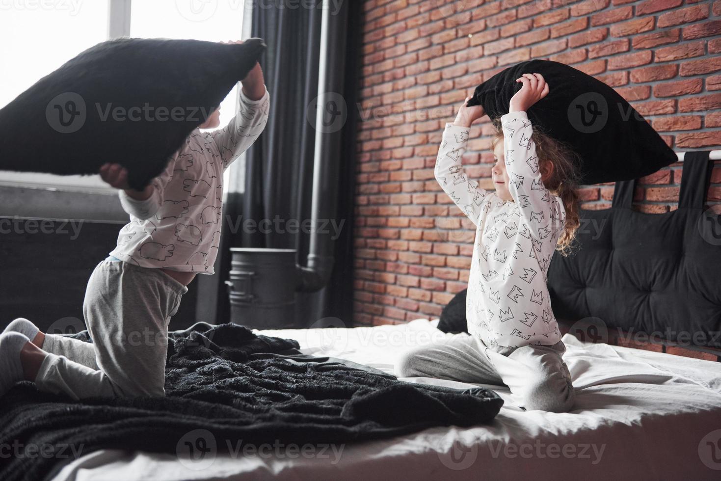 Naughty children Little boy and girl staged a pillow fight on the bed in the bedroom. They like that kind of game photo