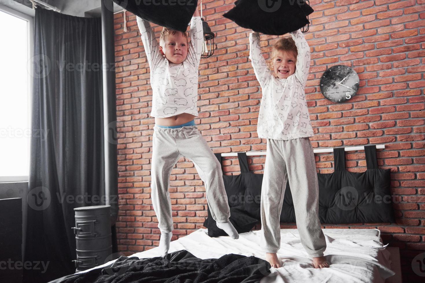 Naughty children Little boy and girl staged a pillow fight on the bed in the bedroom. They like that kind of game photo