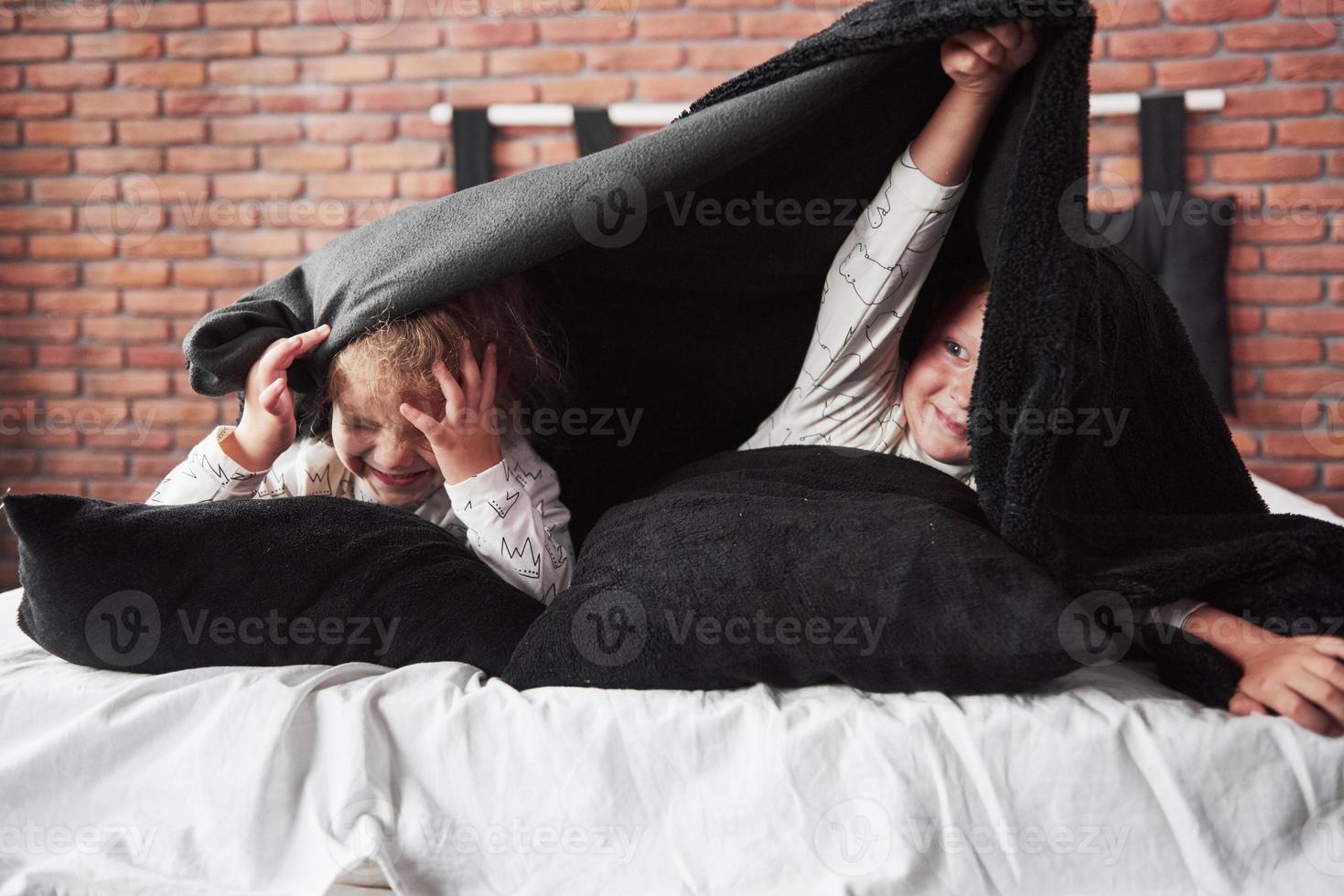 Little children, boy and girl laying and playing with pillows on the bed cover with a blanket photo