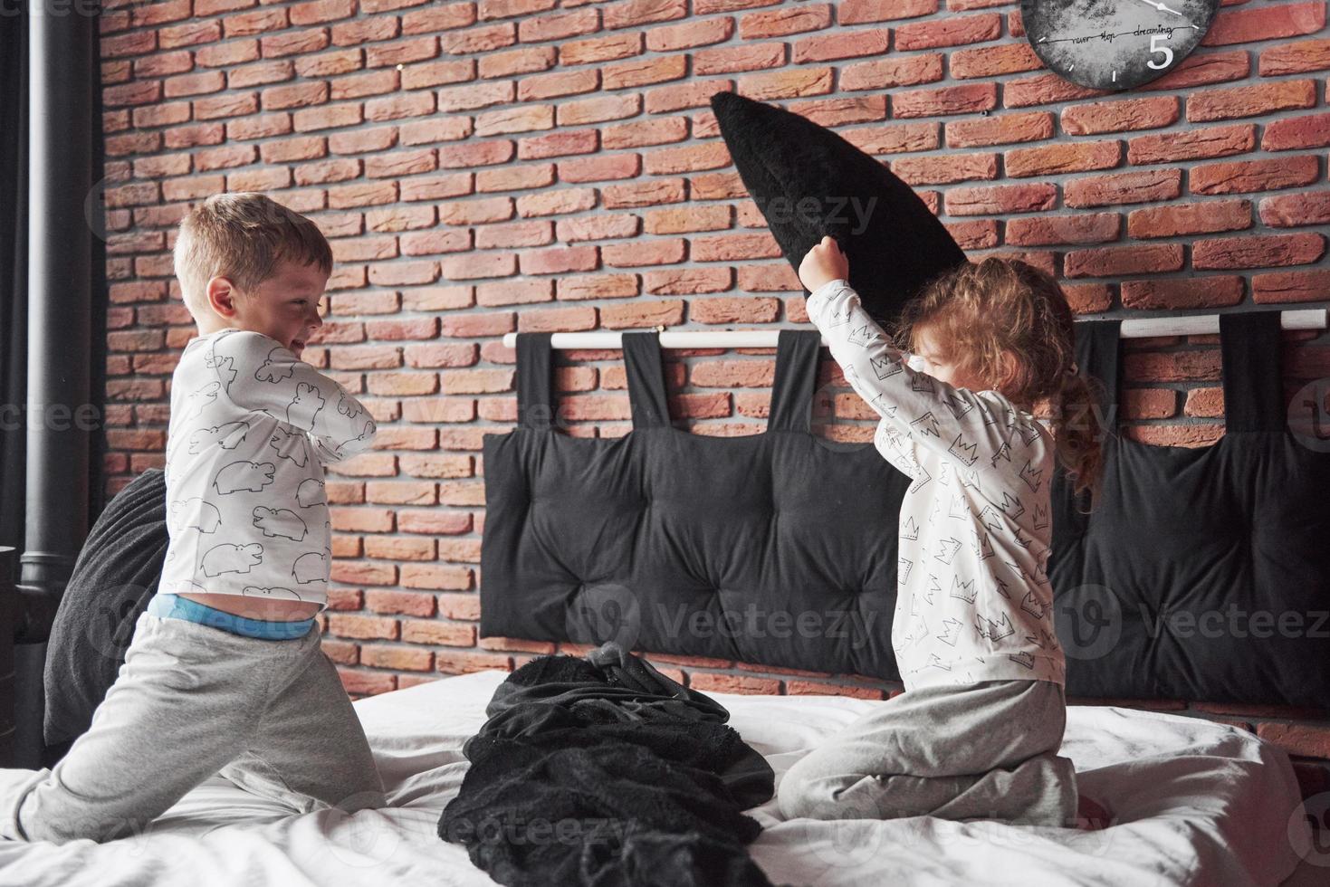 Naughty children Little boy and girl staged a pillow fight on the bed in the bedroom. They like that kind of game photo