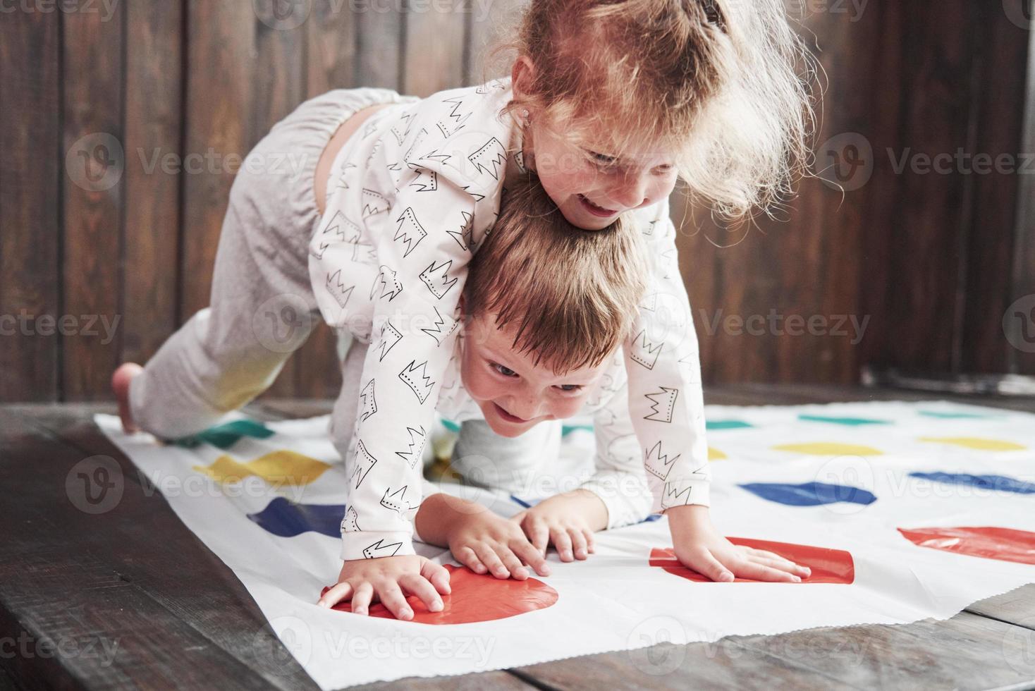 Two of happy children playing at twister in house. Brother and sister have a fun time in holiday photo