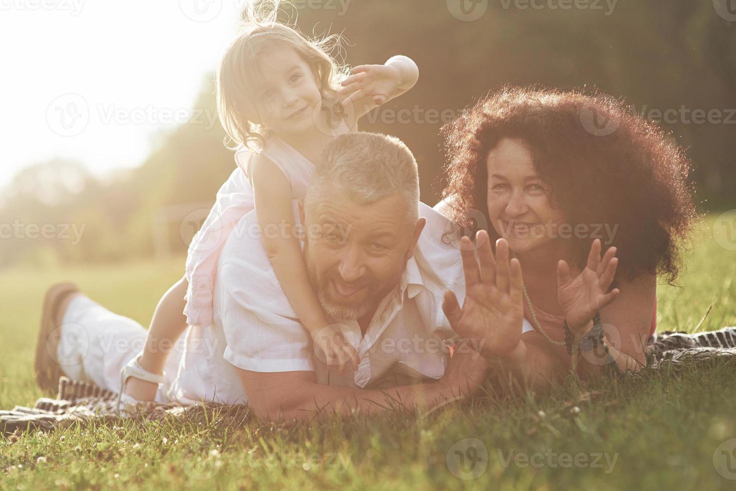una linda niña pasa tiempo con su amado abuelo y abuela en el parque. hicieron un picnic en el pasto foto