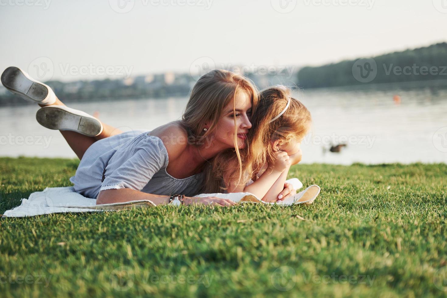 atractiva madre joven feliz acostado con su linda hija en el césped en el parque. foto