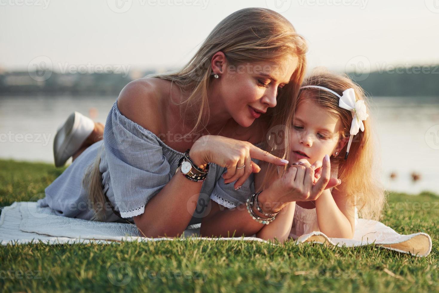 Attractive happy young mother lying with her cute daughter on the grass in the park. photo