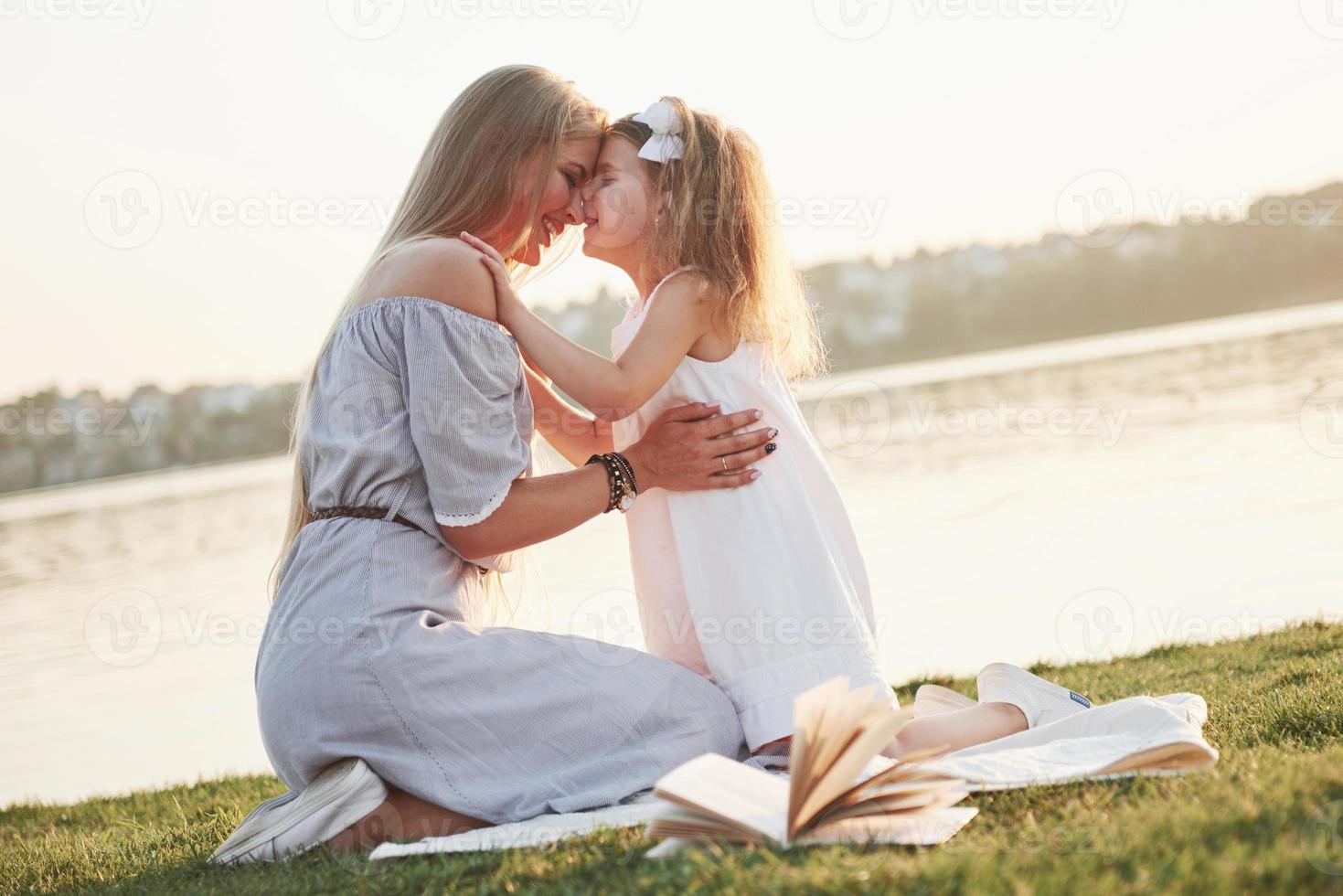 Madre joven feliz con una hija juguetona en un parque cerca del agua foto