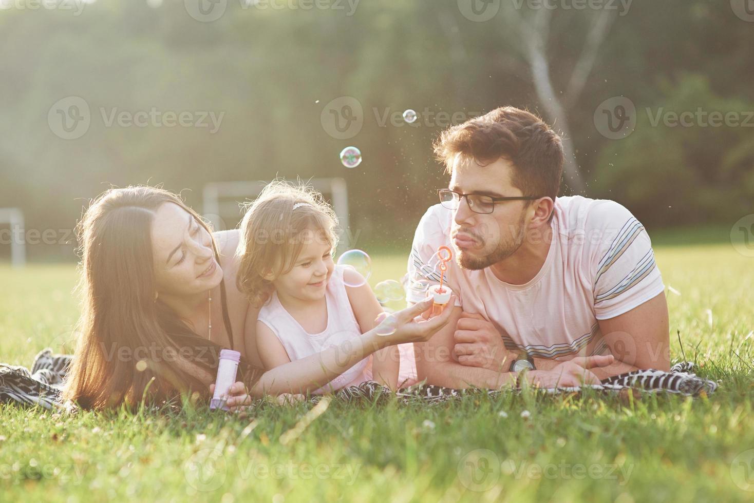 madre y padre pasan tiempo juntos felizmente. Hija juega con sus padres al aire libre durante la puesta de sol foto