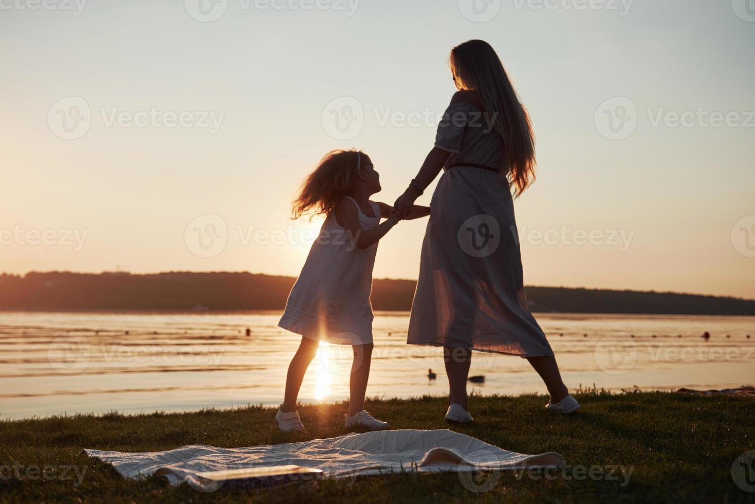 mamá juega con su bebé en vacaciones cerca del océano, siluetas al atardecer foto