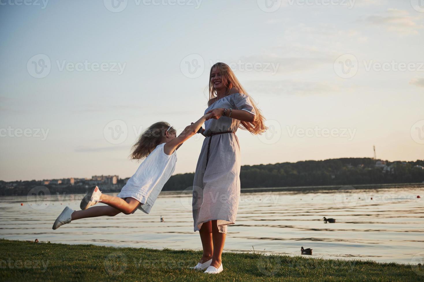 mamá y su pequeña hija juegan en el césped cerca del lago. foto