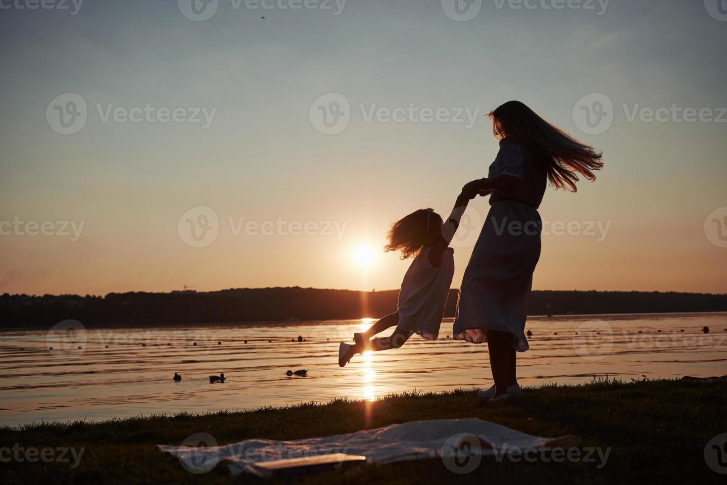 mamá juega con su bebé en vacaciones cerca del océano, siluetas al atardecer foto