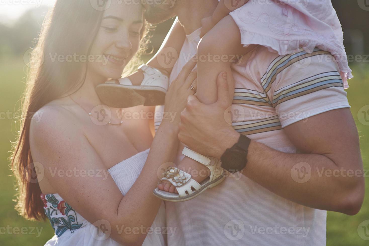 madre y padre pasan tiempo juntos felizmente. Hija juega con sus padres al aire libre durante la puesta de sol foto