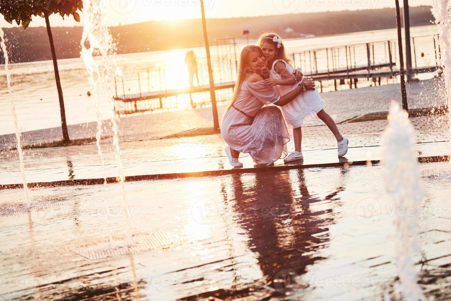 A woman playing with a child near the ocean in the park at sunset photo