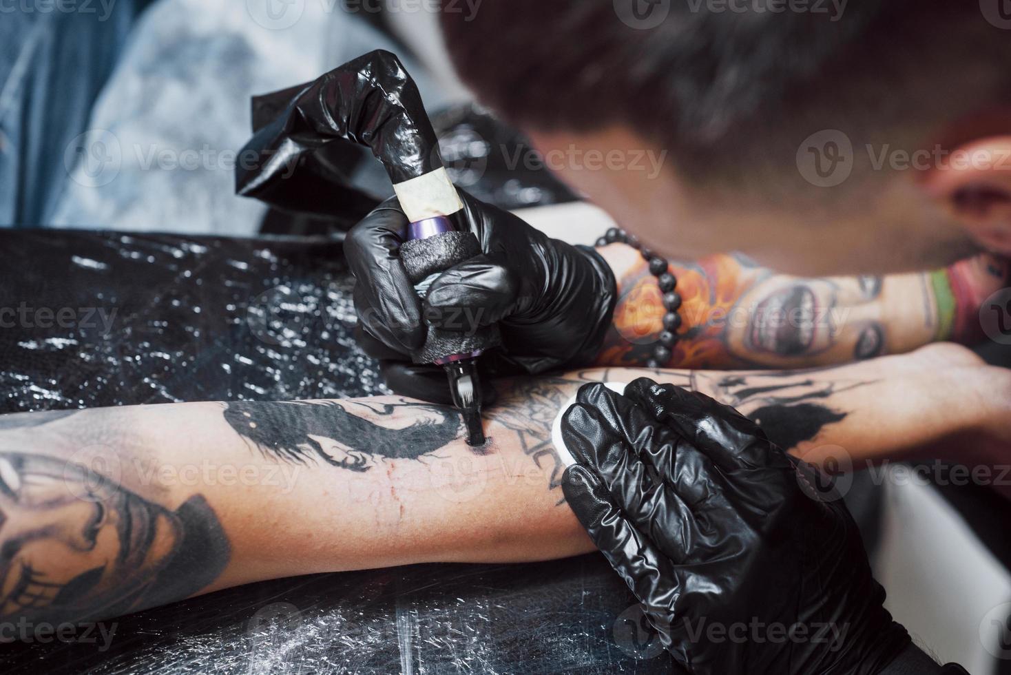 cerrar la máquina de tatuaje. Maestro en guantes negros estériles creando una imagen a mano con ella en el salón foto